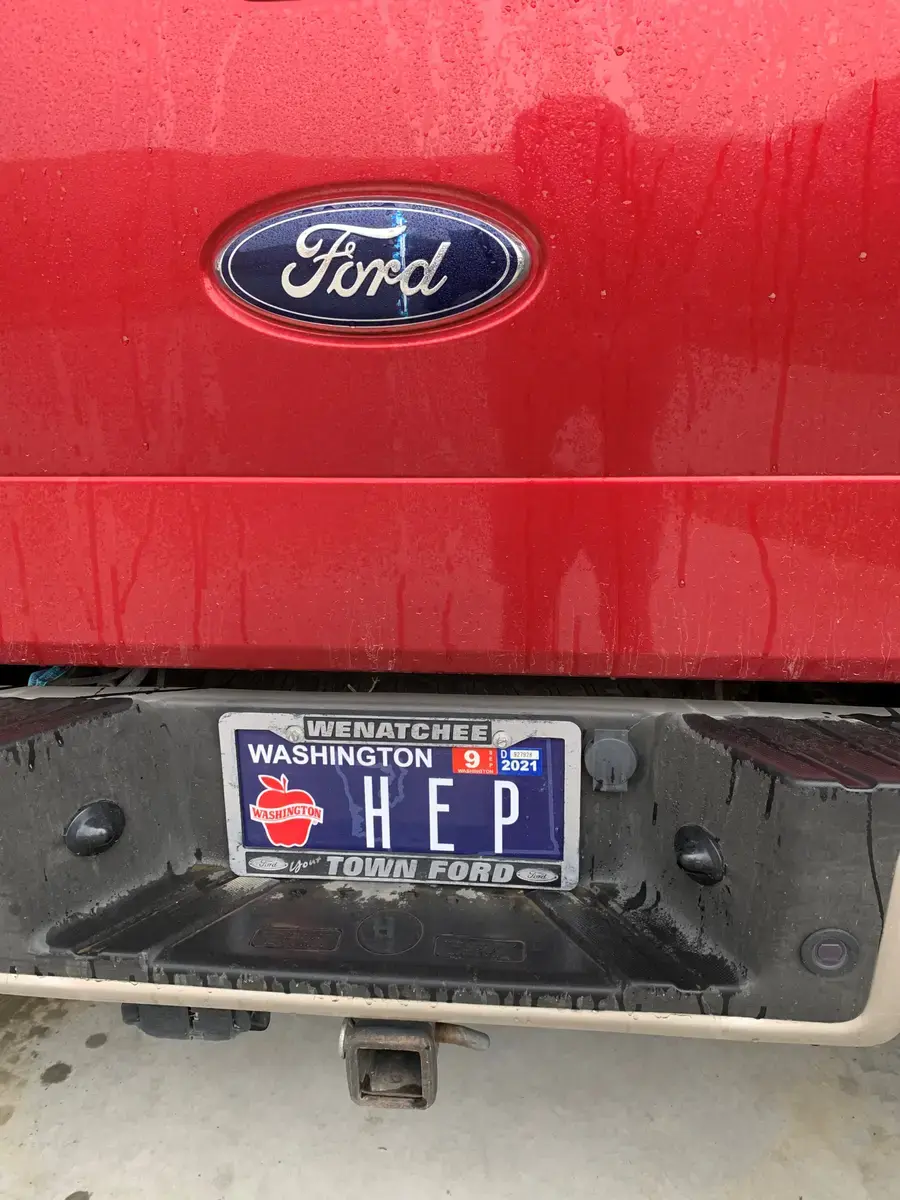 The rain-beaded tailgate of a red Ford pickup with a personalized Washington Apples plate reading HEP in a Town Ford Wenatchee frame