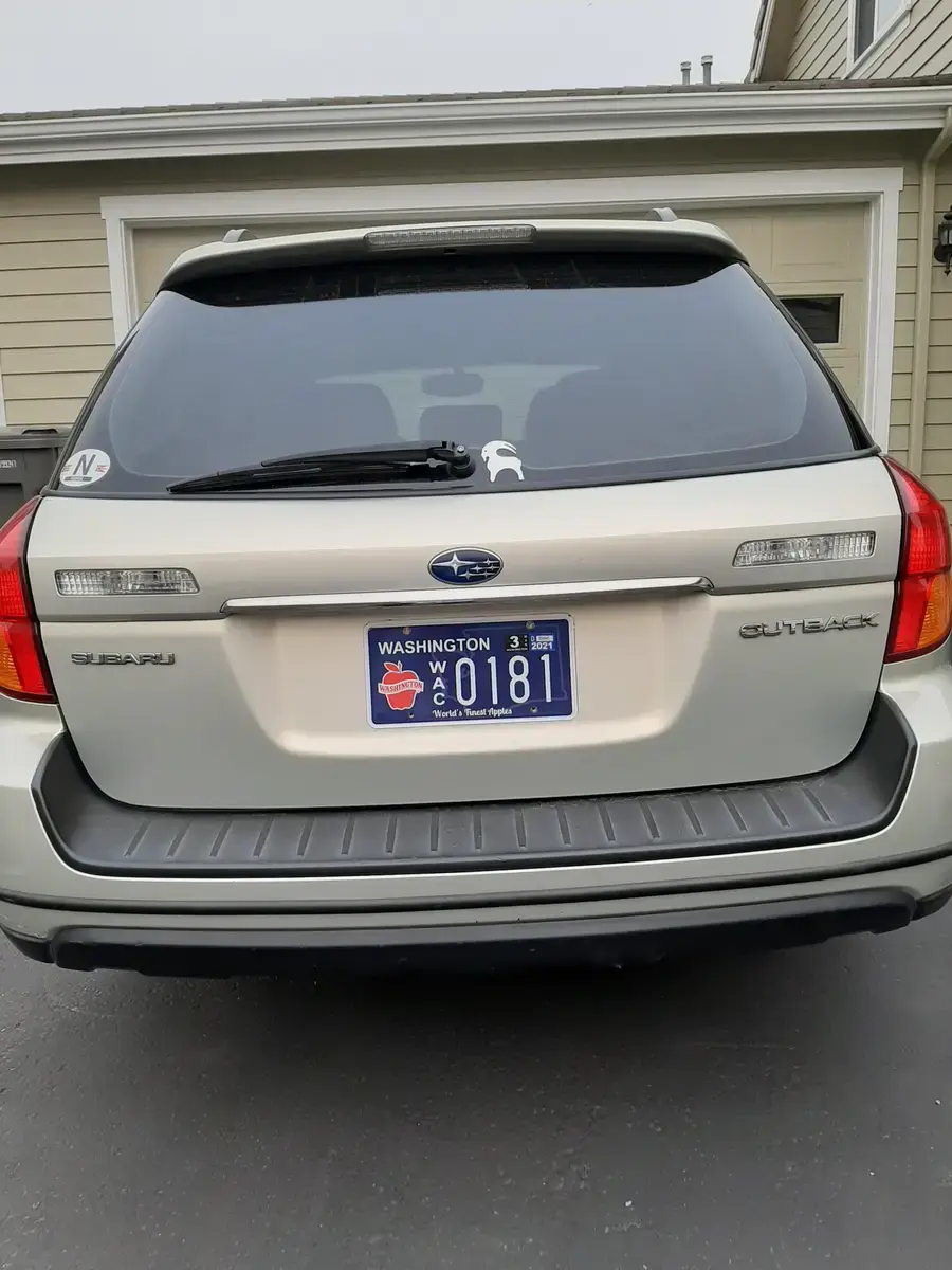 The back of a silver Subaru Outback with a Washington Apples plate, parked beside a house