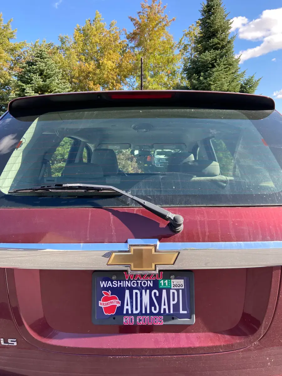 The back of a red Chevrolet with a personalized Washington Apples plate reading ADMSAPL, under autumn trees