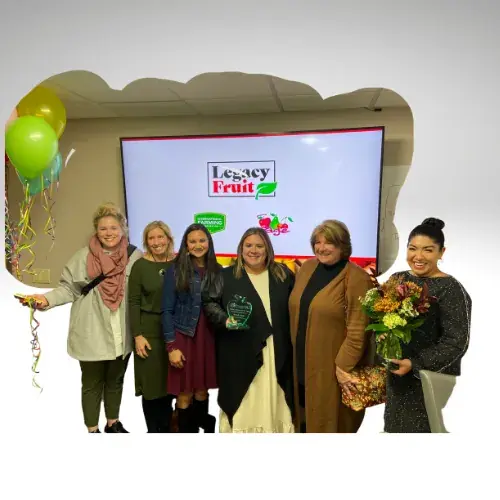A group of women holding awards and flowers in front of a Legacy Fruit screen