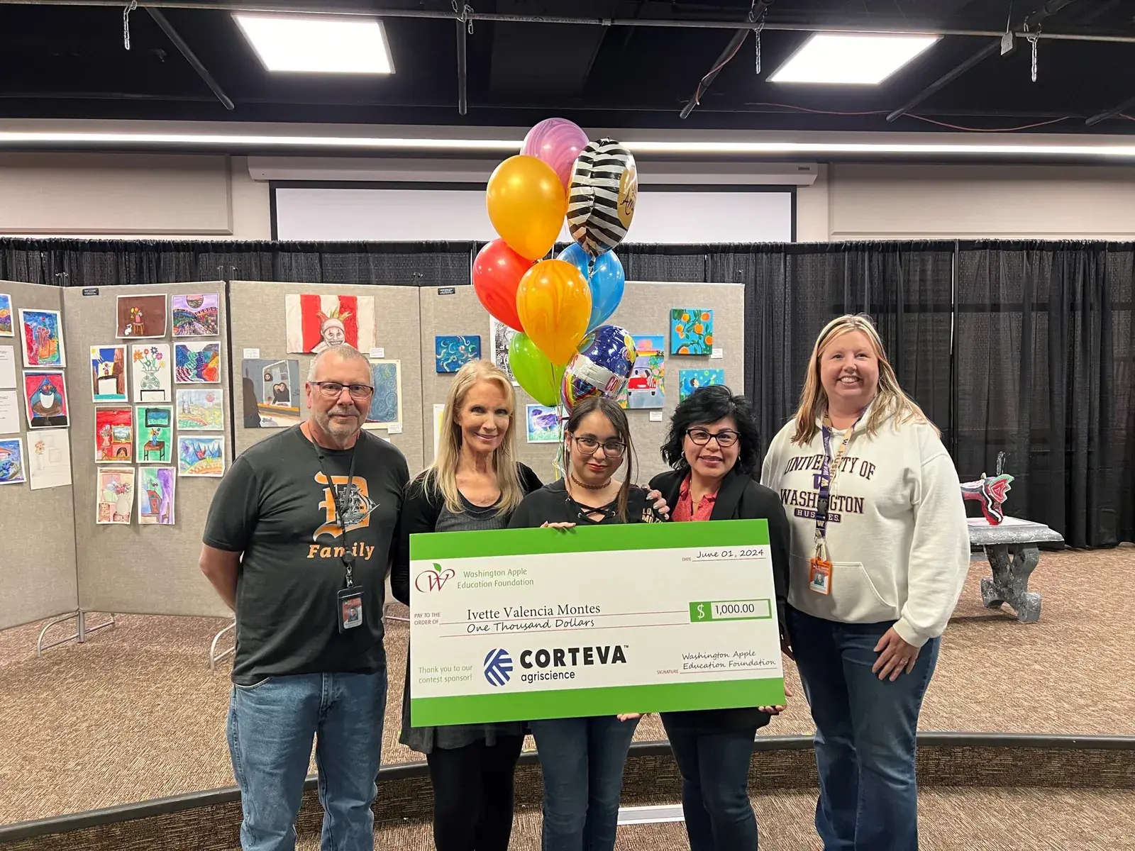Six people holding an oversized Corteva cheque beneath balloons at a school event