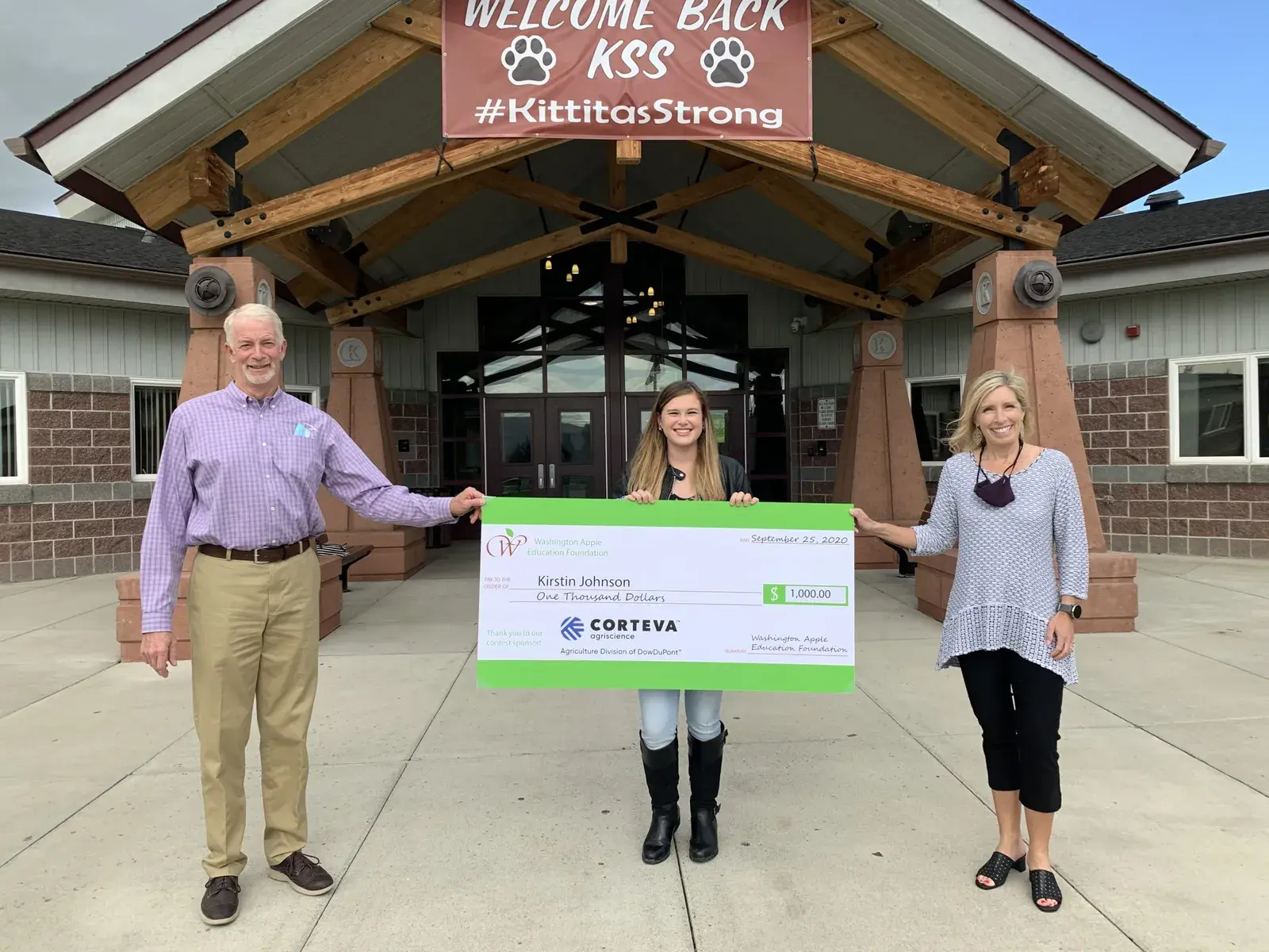 Four people holding an oversized Corteva cheque outside a school entrance