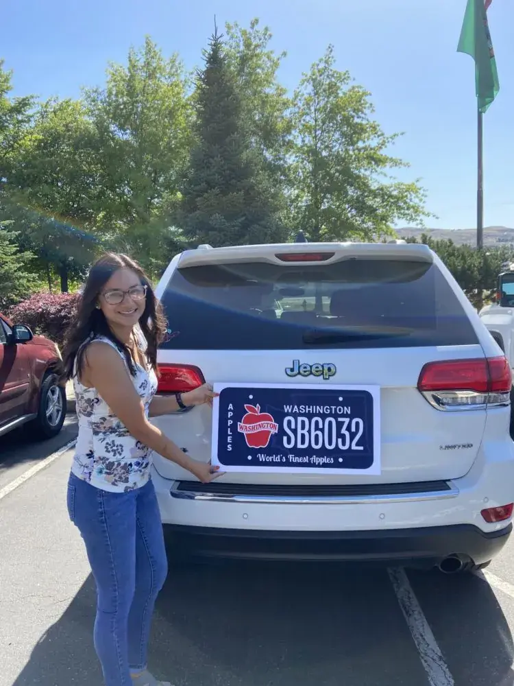 A woman standing beside a car displaying a Washington Apples specialty licence plate