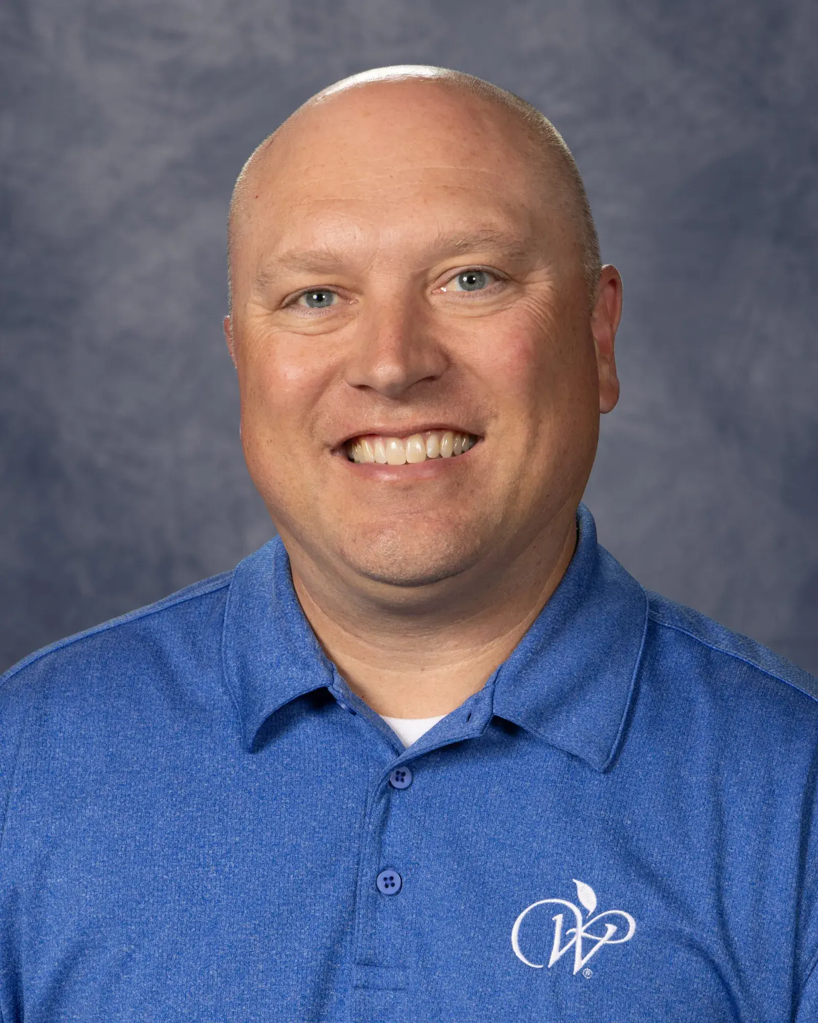 Nate Fulton, in a blue polo shirt, in a studio portrait against a grey backdrop