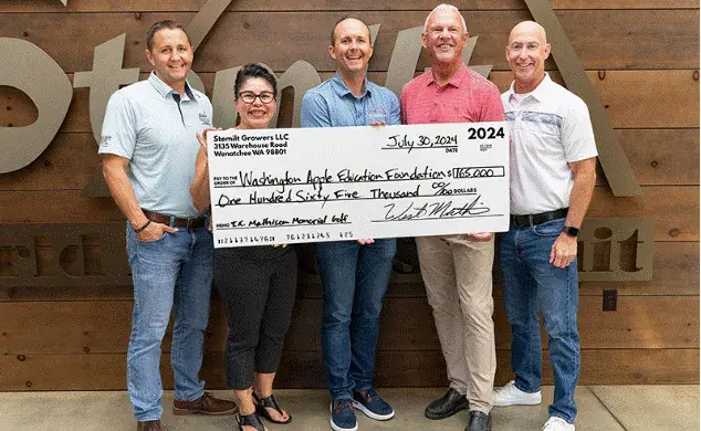 Five people holding an oversized ceremonial cheque in front of a Stemilt sign