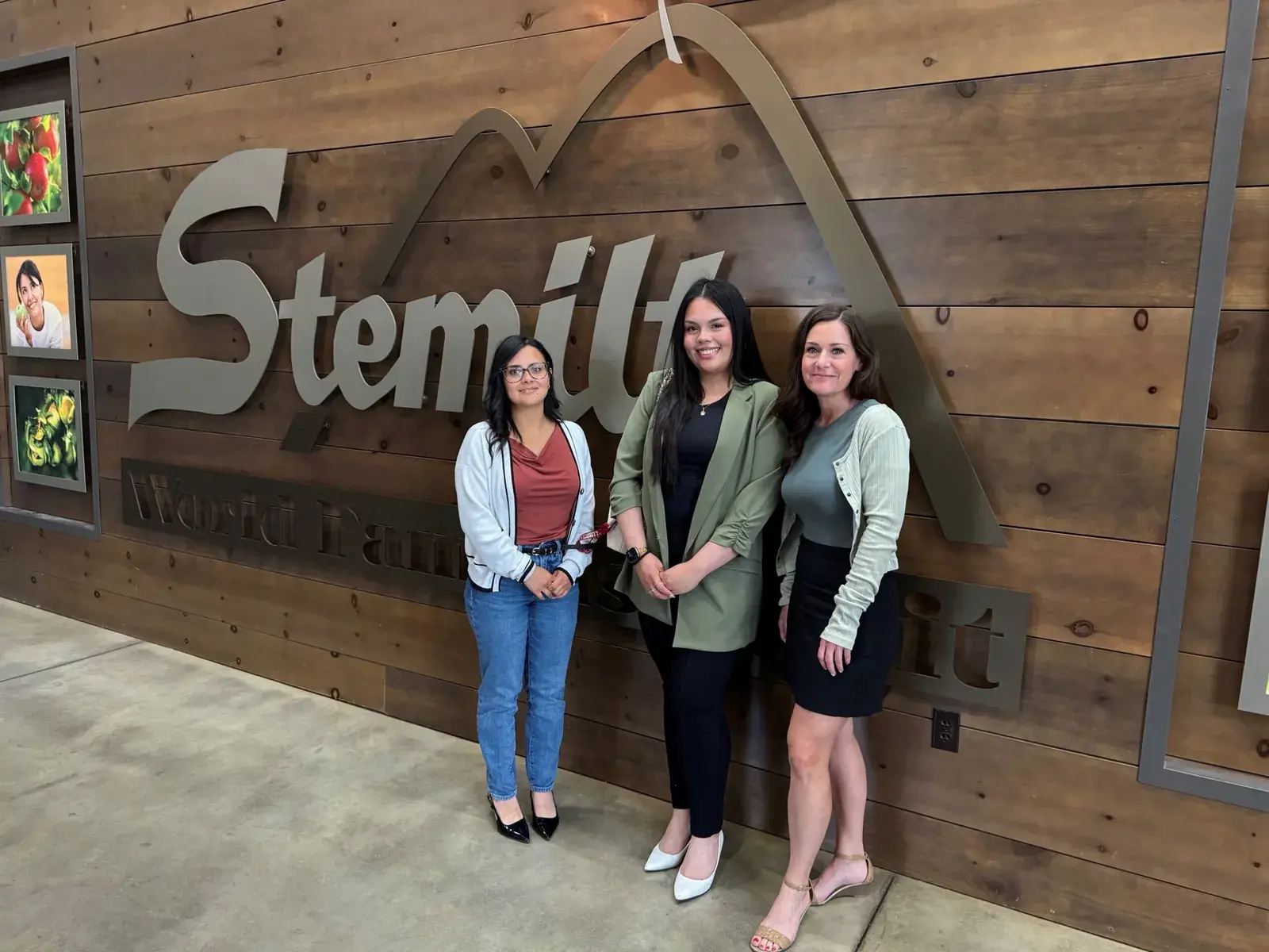 Three students standing in front of a large wooden Stemilt sign