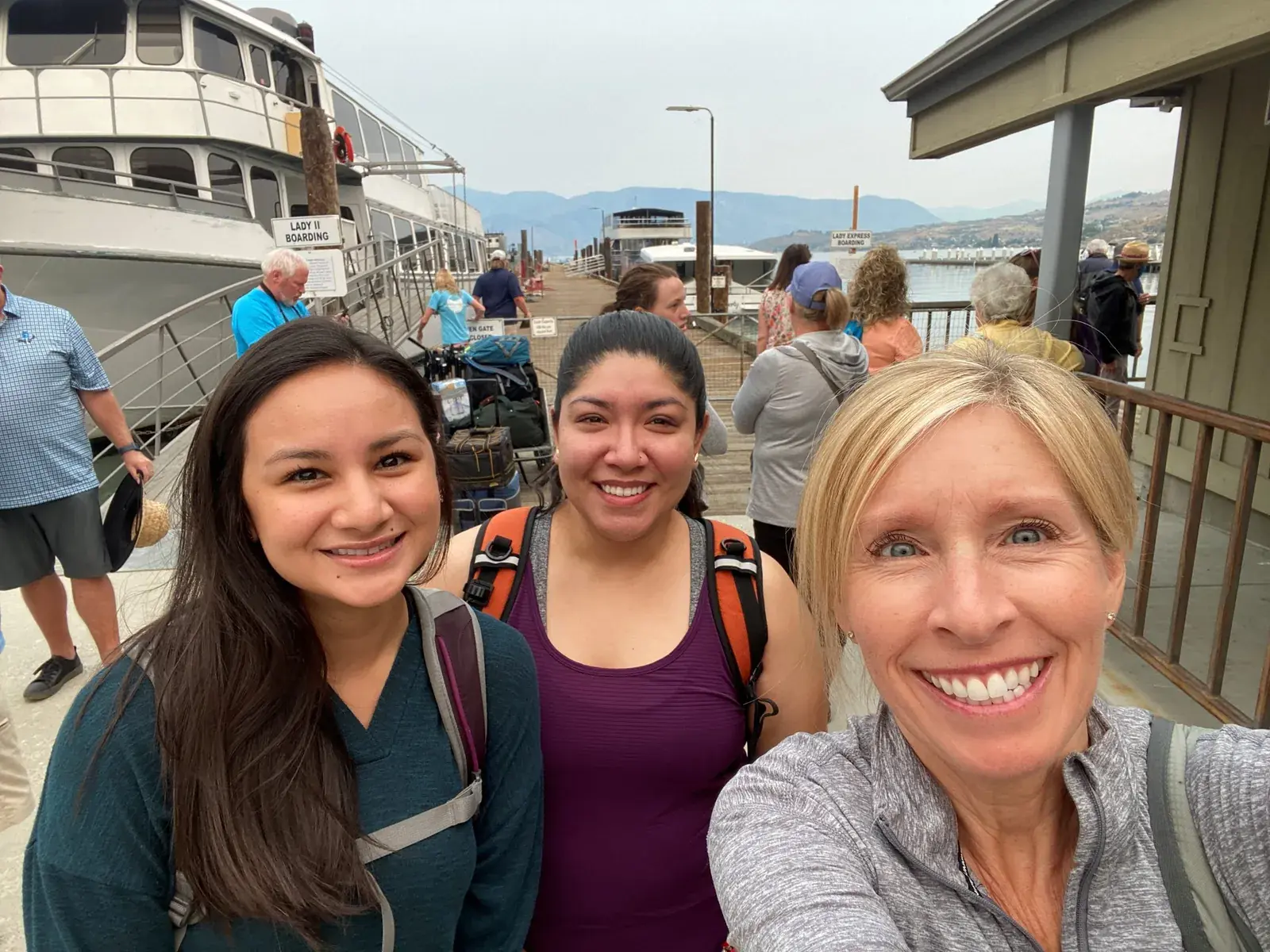 Three women taking a selfie outdoors at a waterfront event