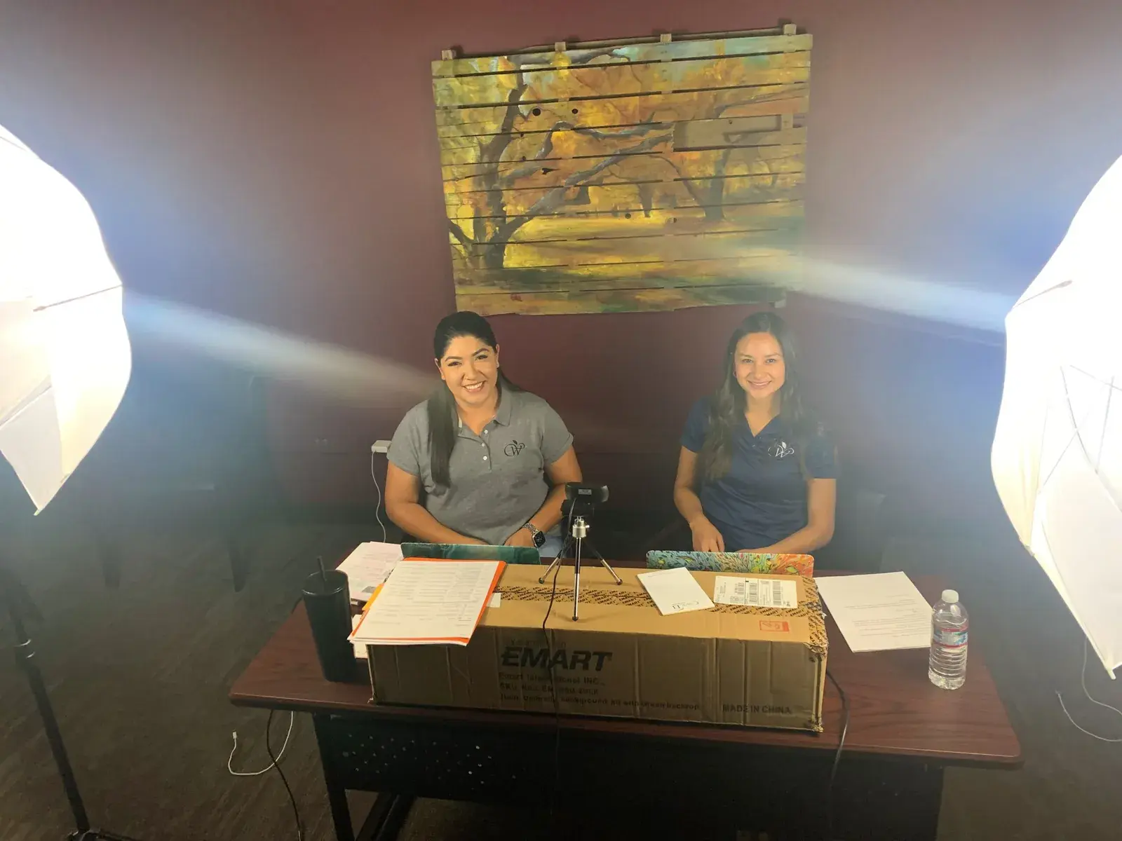 Two women seated at a table behind studio lighting during a recorded presentation