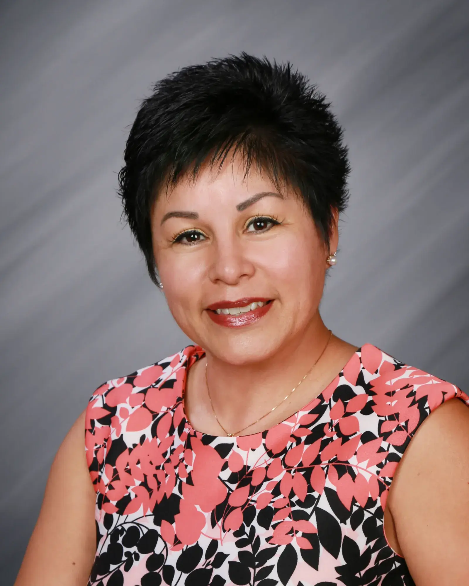 A woman with short dark hair in a floral top, in a studio portrait