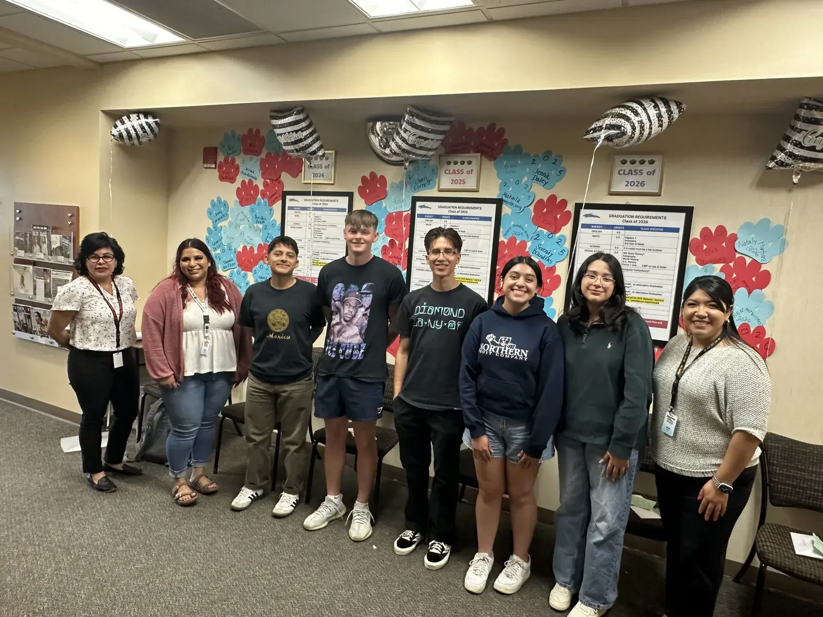 Students and staff posed together in a classroom decorated with paper flowers