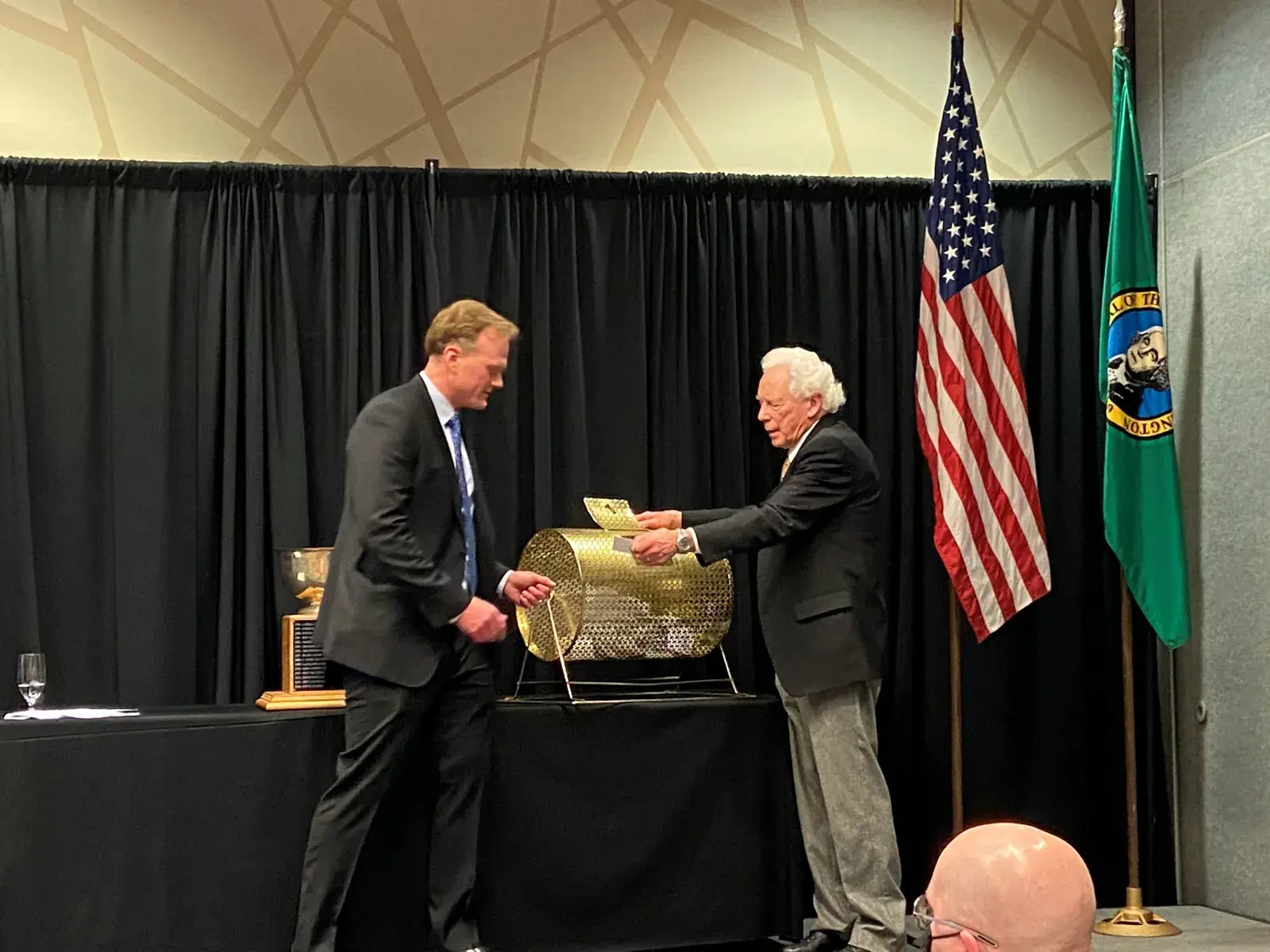 Two men shaking hands on an auction stage in front of United States and Washington state flags