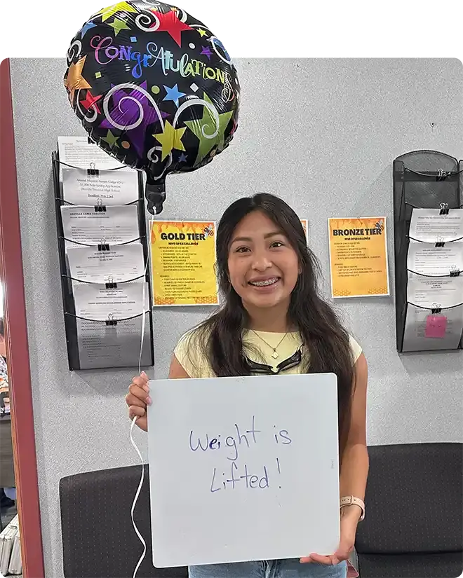 A smiling scholarship recipient with a balloon and a sign that says what a difference it will make to her