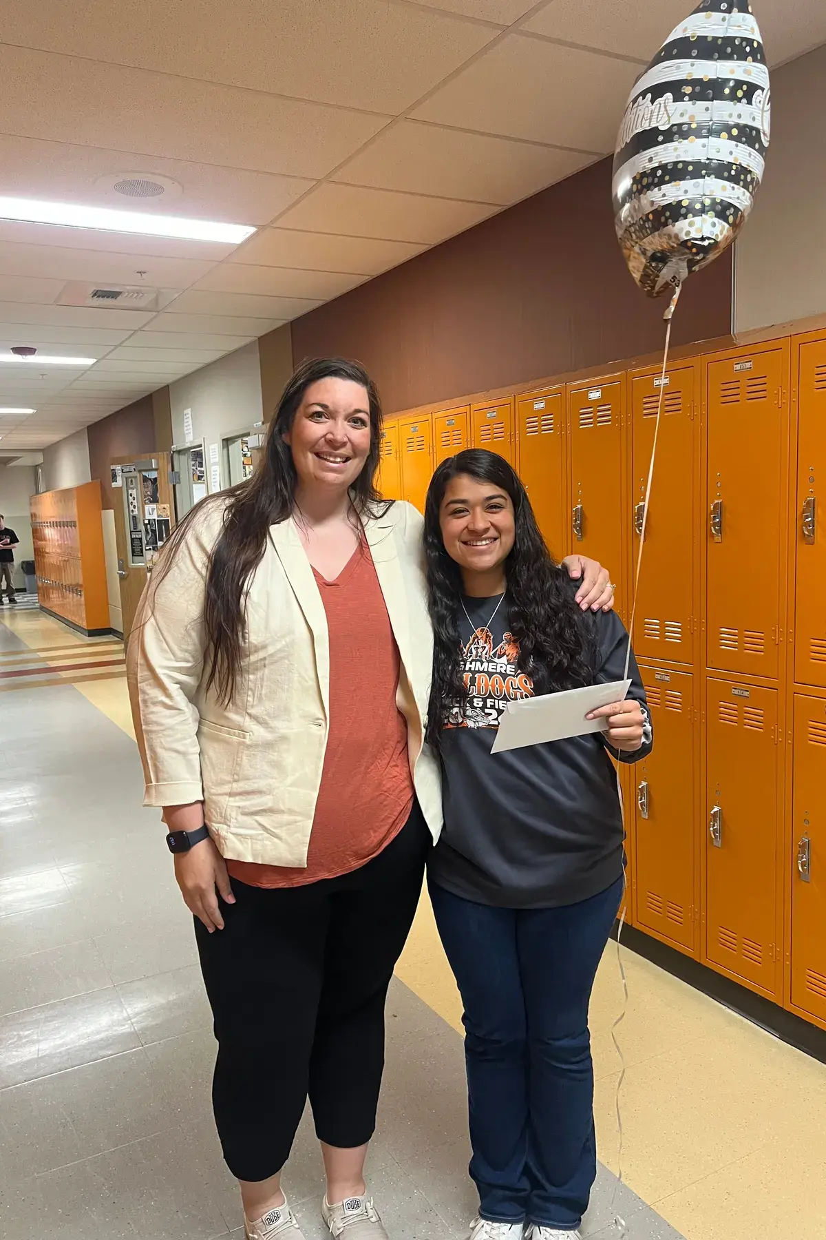 A WAEF scholarship recipient holding her award letter in a school hallway, a counselor's arm around her shoulders