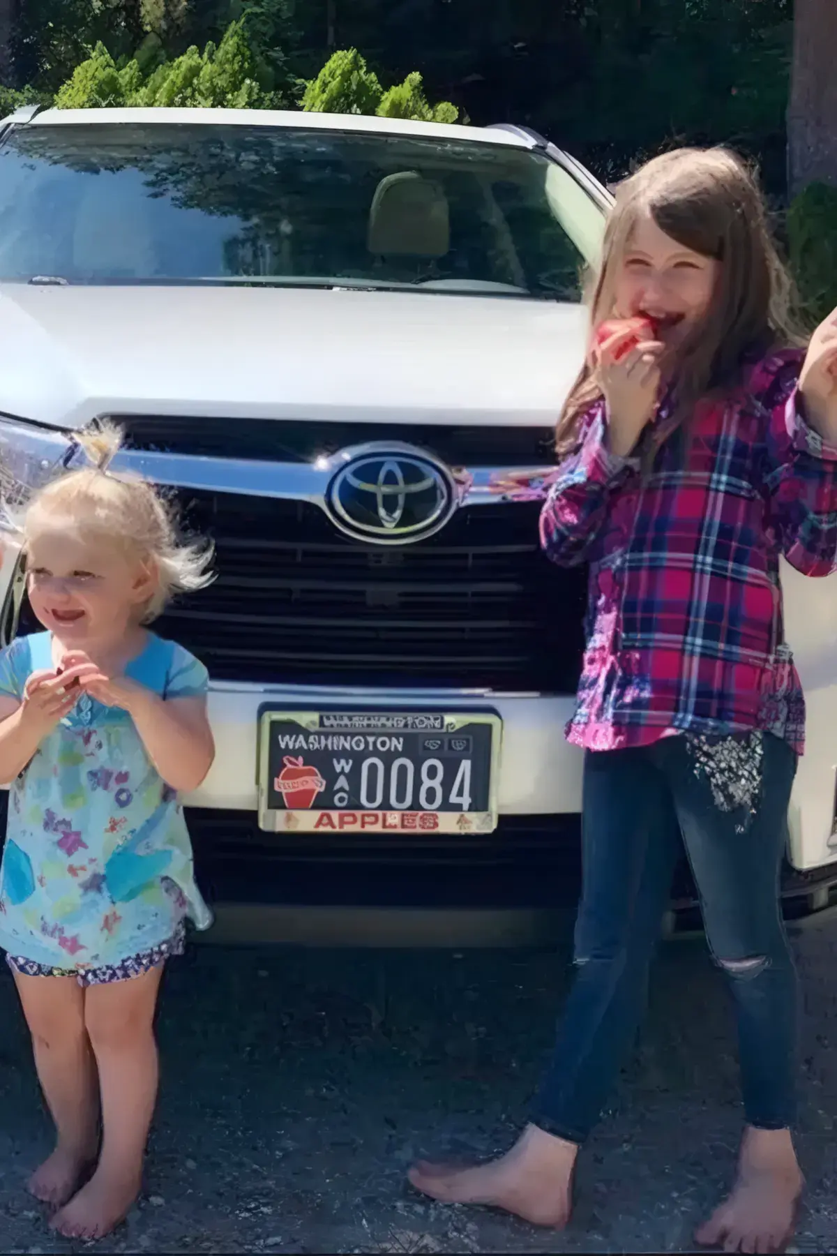 Children eating apples in front of a car wearing the Washington Apples license plate