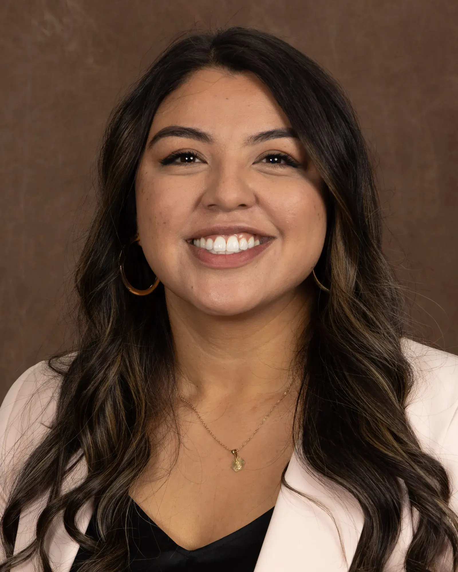 Lupe Villasenor, in a black top and pale blazer, smiling in a studio portrait