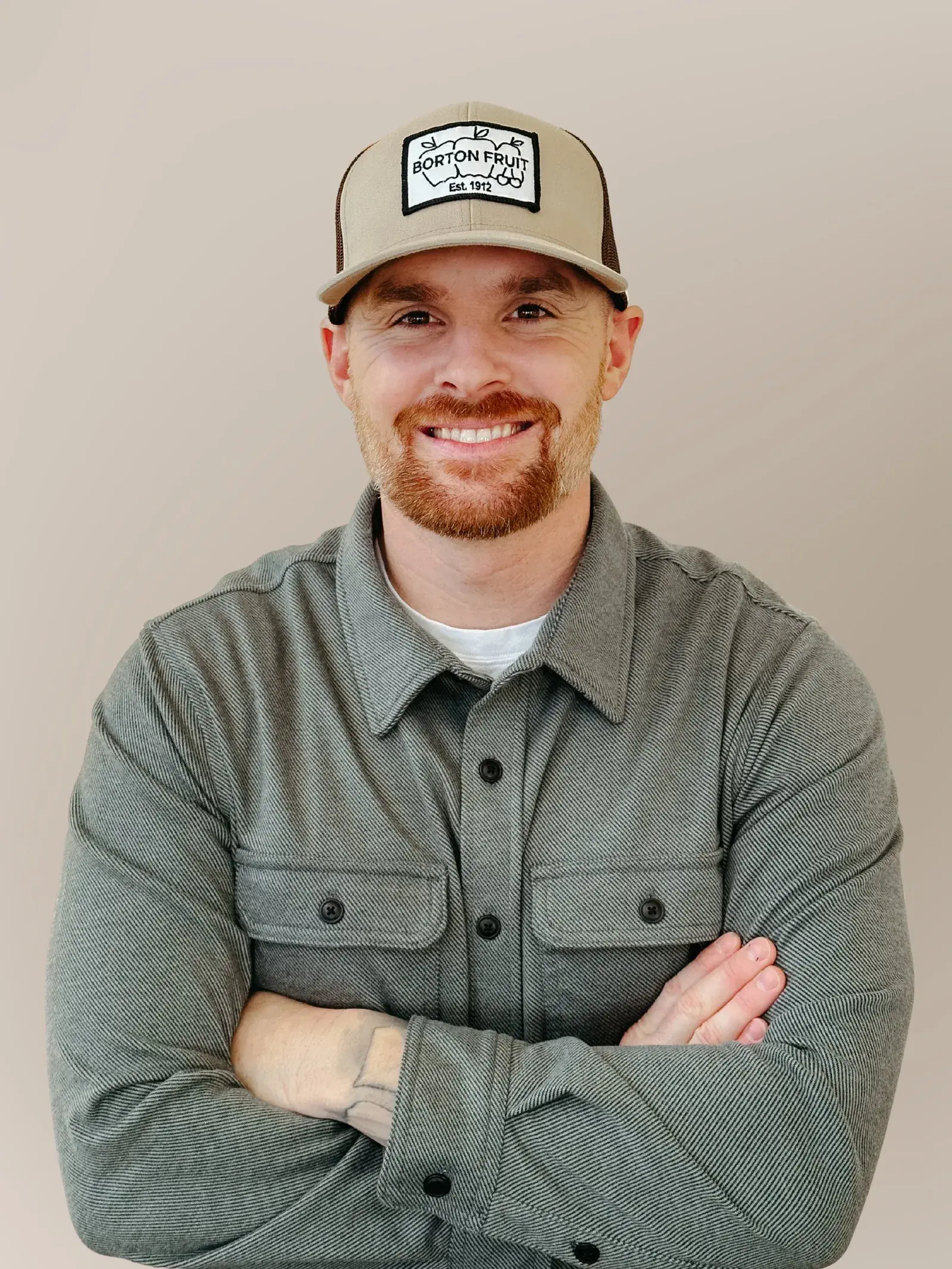 Drew Belton, in a cap and green button-down shirt, standing outdoors with his arms folded