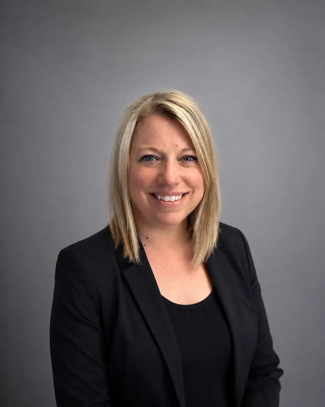 Jenny Faletto, in a black blazer with shoulder-length blonde hair, in a studio portrait