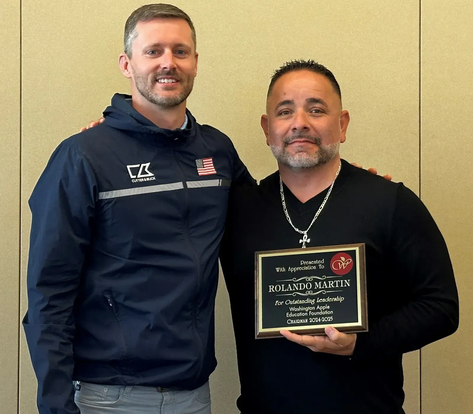Two men standing side by side, one holding an engraved award plaque