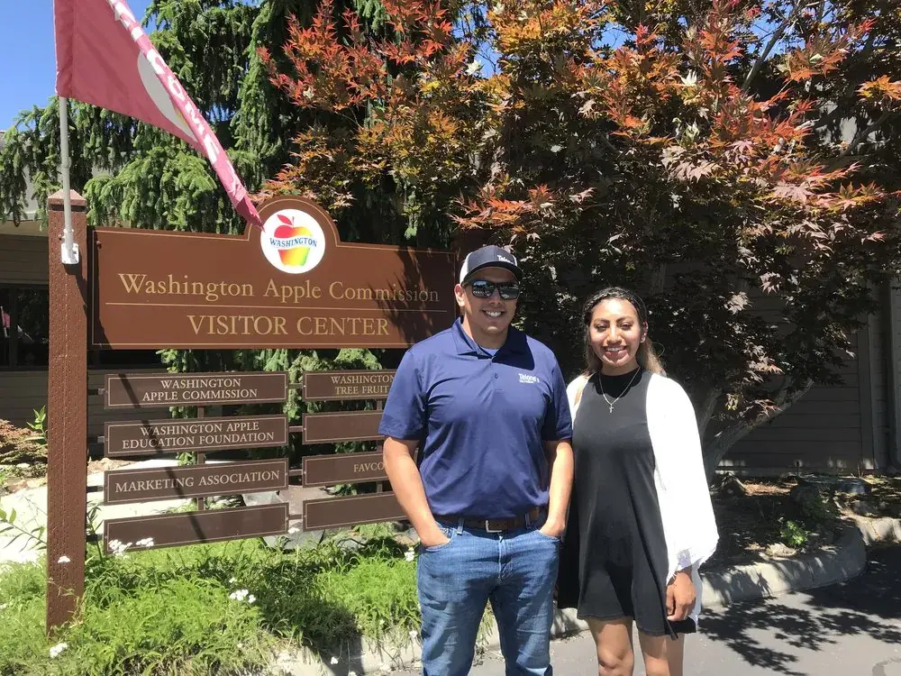 A man and a woman standing beside the Washington Apple Commission visitor centre sign